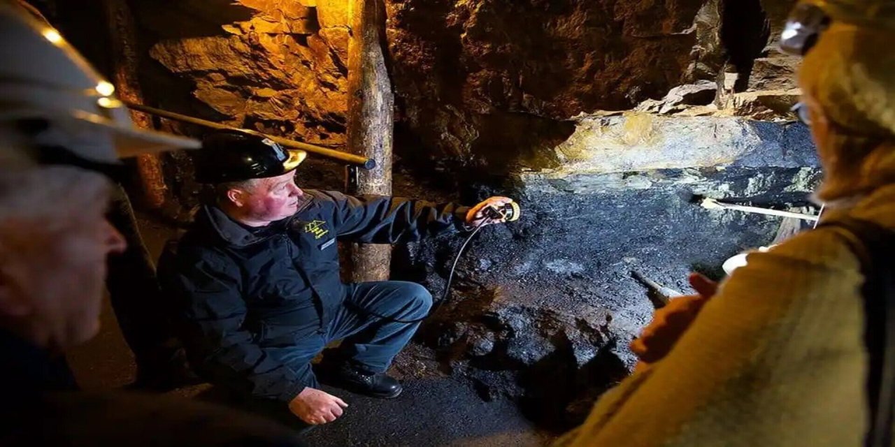 tour guide and participants looking through an opening of a mine. Surrounded by rock. Man looking out of gap. 