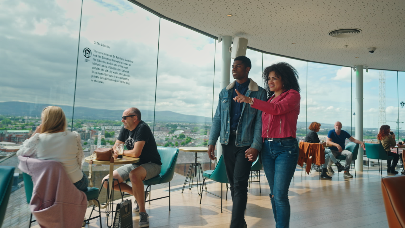 couple walking through the bar at guinness storehouse a man and a woman in the guinness bar walking through, other people sitting down at tables