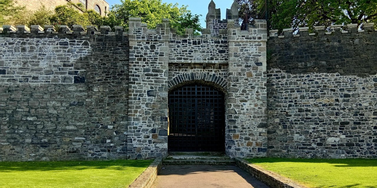 Black medieval gate surrounded by old grey brick wall